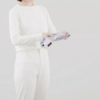 Person wearing a white outfit holding a product against a plain background